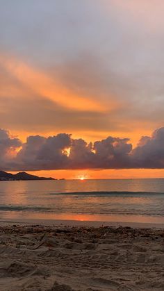 the sun is setting over the ocean with clouds in the sky and on the beach