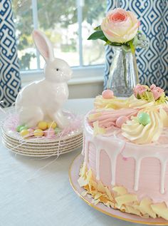 there is a cake on the table with flowers in the vase and an easter bunny figurine next to it