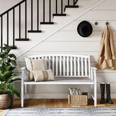 a white bench sitting under a stair case next to a wooden hand rail and potted plant