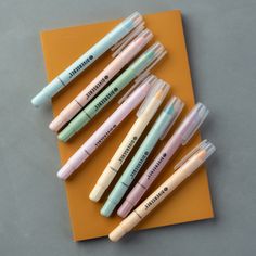 five pens sitting on top of an orange piece of paper next to each other with writing on them