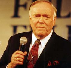 an older man holding a microphone in his right hand and wearing a suit with a red tie