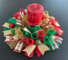 a red candle sitting on top of a christmas wreath with burlocks and ribbons