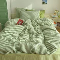 an unmade bed with green and white striped comforter, pillows, and pictures on the wall