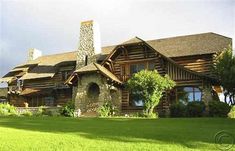 a large log house with a clock tower in the front yard and green grass on both sides