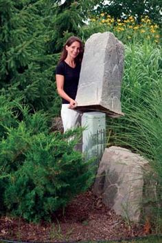 a woman standing next to a large rock in the grass