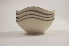 four white bowls stacked on top of each other in the shape of wavy lines, against a gray background