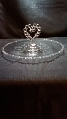 a glass cake plate sitting on top of a black cloth covered table with a heart shaped center piece