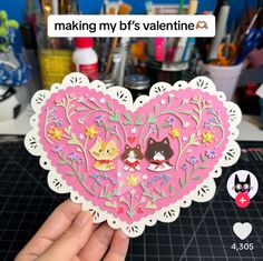 someone holding up a heart shaped cutout in front of a table full of craft supplies