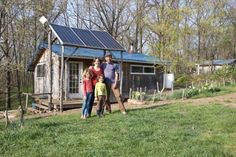 three people standing in front of a small house with solar panels on it's roof