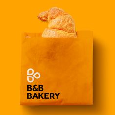 an orange paper bag with a pastry in it on a yellow background that says b & b bakery