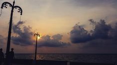 the sun is setting over the ocean and people are standing on the pier looking out at the water