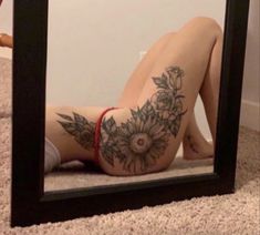 a woman laying on the floor in front of a mirror with flowers tattooed on it