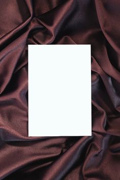 an empty card is placed on top of a brown satin material with a white square in the middle