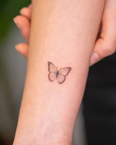 a small butterfly tattoo on the wrist is shown in black and grey ink, with an outline of a butterfly