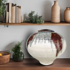 a vase sitting on top of a wooden shelf next to two other vases and books