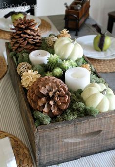 a wooden box filled with pine cones and candles on top of a dining room table