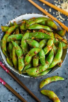 a bowl filled with green beans next to chopsticks and seasoning on the side