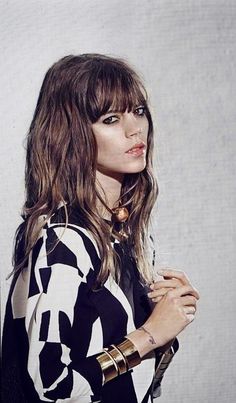 a woman with long hair standing in front of a white wall wearing a black and white shirt