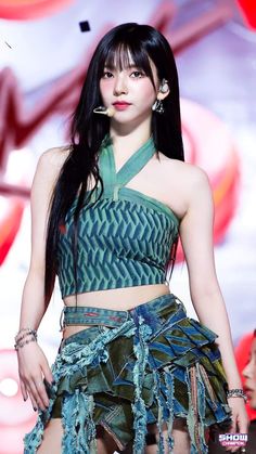 a woman with long black hair wearing a green top and skirt on the catwalk