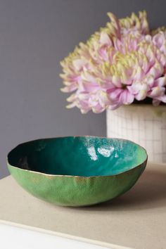 a green bowl sitting on top of a counter next to a vase with flowers in it