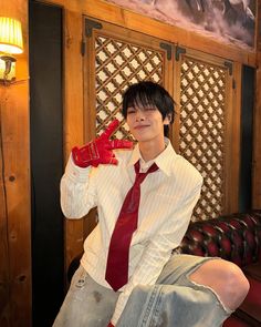 a young man wearing a red tie and white shirt sitting on a couch with his hands in his pockets