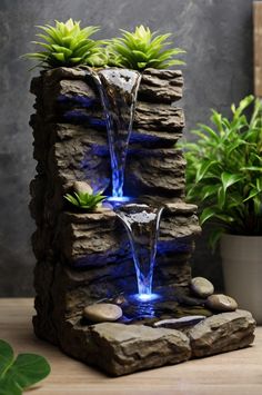 an outdoor fountain with blue lights and rocks on the ground next to potted plants