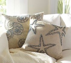 three pillows on a couch in front of a window with an ocean themed throw pillow