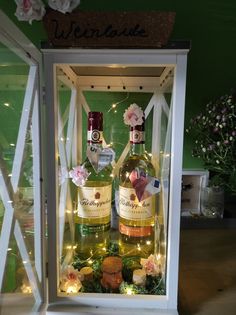 two bottles of wine in a display case with fairy lights on the bottom and flowers at the top