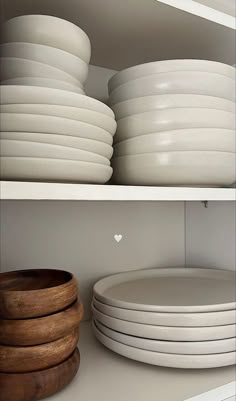 white plates stacked on top of each other in a kitchen shelf next to a wooden bowl