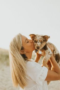 a woman kissing her dog on the beach with sand in the backgroung