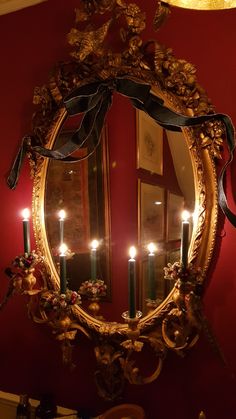 a mirror that has some candles on it in front of a red wall with two mirrors