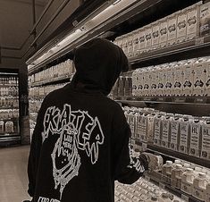 a person in a black hoodie is looking at cans of soda and milk on shelves