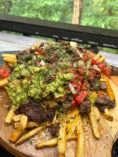 a wooden platter filled with fries covered in guacamole and toppings