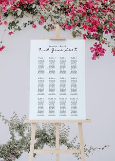 an easel with a seating chart on it in front of pink flowers and greenery