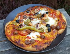 a pizza sitting on top of a black plate covered in cheese and toppings next to a green pepper