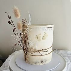 a white cake decorated with dried flowers and baby's footprints