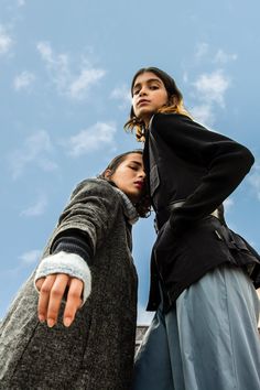 two women standing next to each other in front of a blue sky with white clouds