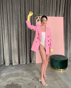 a woman standing in front of a pink backdrop holding a flower and wearing yellow gloves