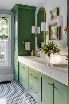 a bathroom with green walls and white counter tops, gold trimming on the mirror