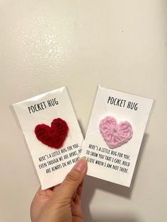 someone holding up two small cards with crochet hearts on them that say pocket hug and pocket hug