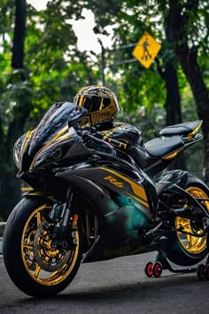 a man riding on the back of a black and yellow motorcycle down a street next to trees