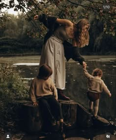 a woman holding the hand of two small children on a tree stump near a body of water