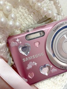 a pink camera sitting on top of a white blanket next to a teddy bear and pearls