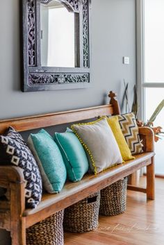 a wooden bench sitting next to a window filled with lots of different colored pillows on top of it