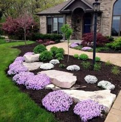 landscaping in front of a house with purple flowers and rocks on the ground next to it