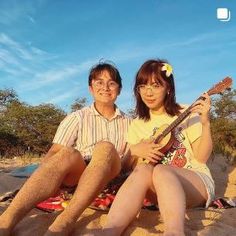 two people are sitting on the sand and one is holding a ukulele guitar