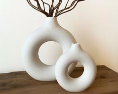 two white vases sitting on top of a wooden table next to each other with branches in them