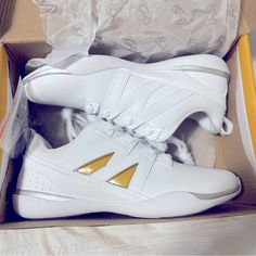 a pair of white and gold sneakers in a box with the shoe laces down