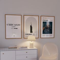 three posters hang on the wall above a white dresser with a lamp next to it