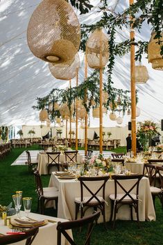 tables and chairs are set up under the tent for an outdoor wedding reception with hanging lanterns